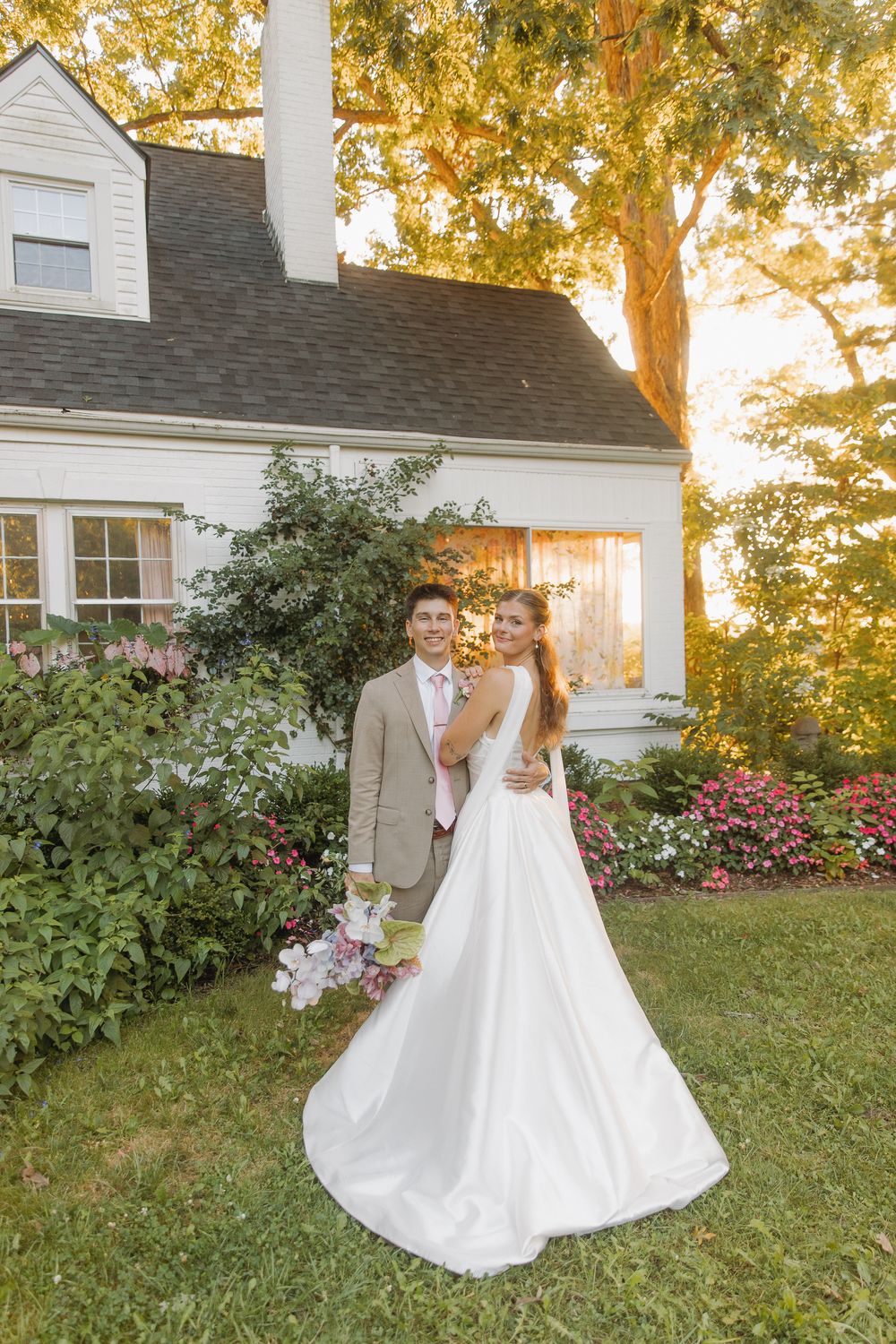 Newlywed couple poses together during golden hour in front of a white house with autumn trees in the background in Lexington, Kentucky.