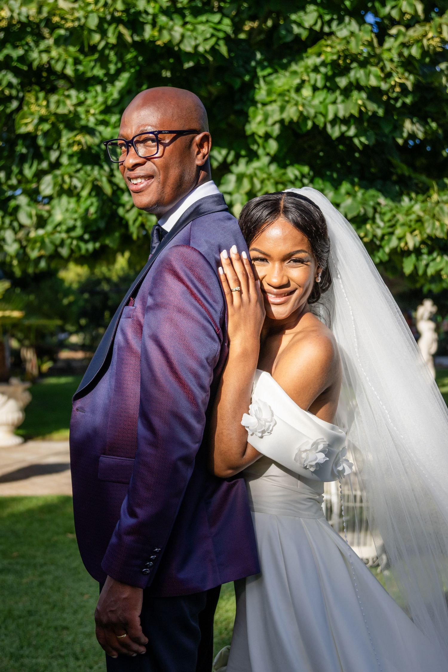 Joyful wedding couple posing together outdoors with lush greenery backdrop.