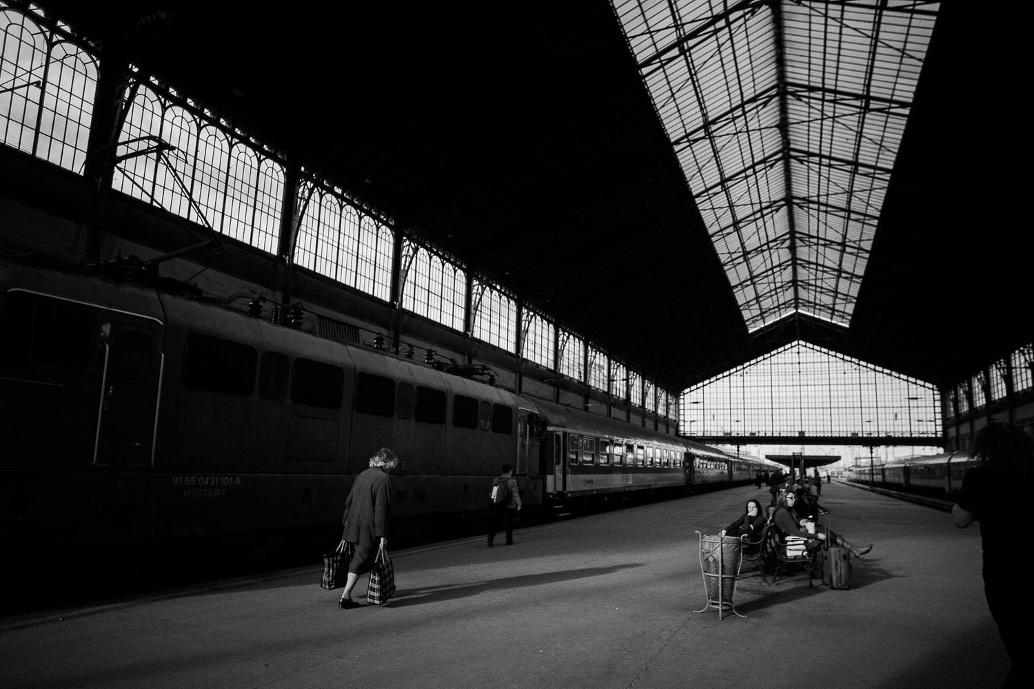 Black and white photograph of a spacious train station interior with natural light streaming through skylight windows.
