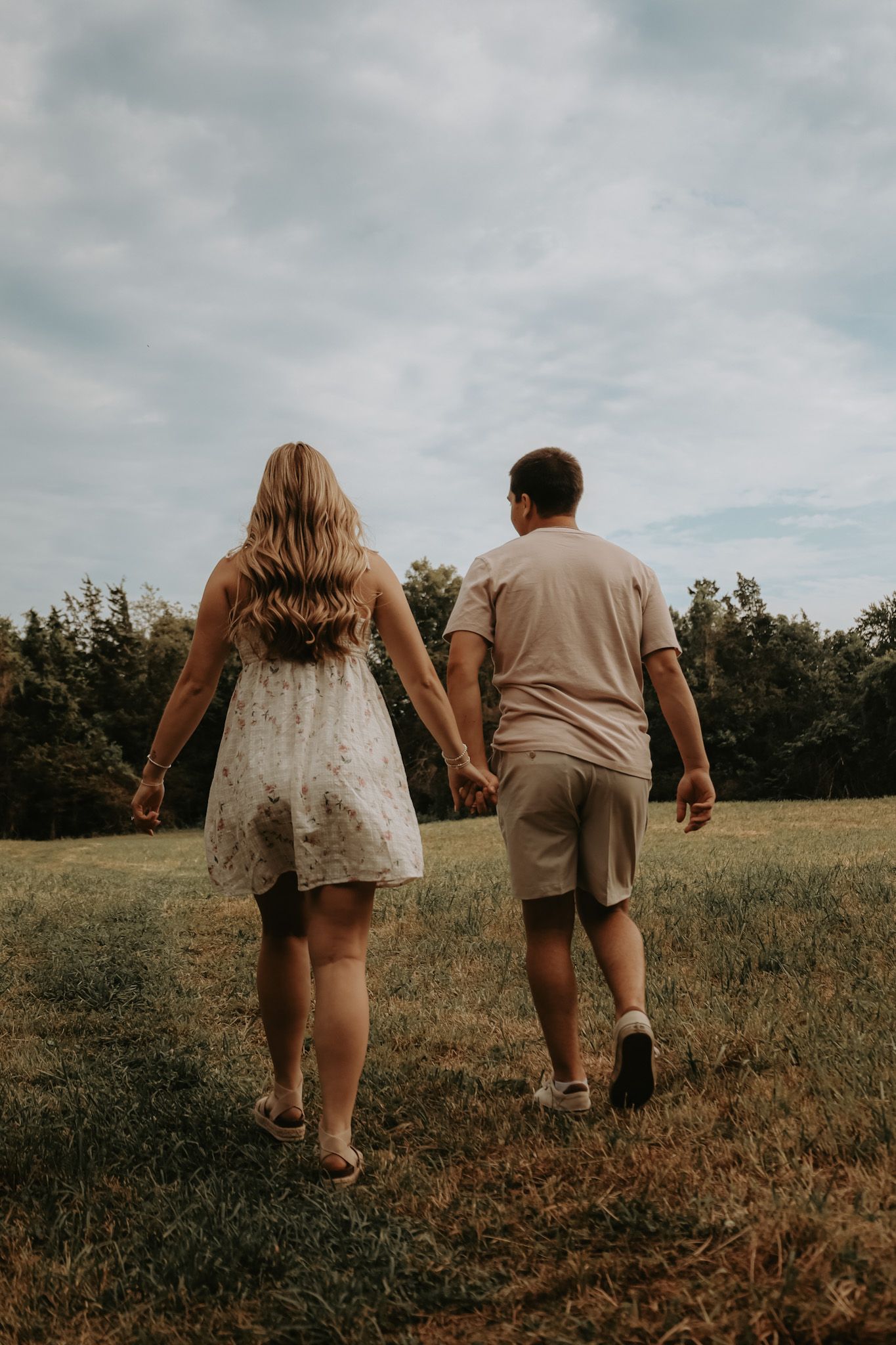 Two people walking hand in hand through a sunny meadow on a cloudy summer day.