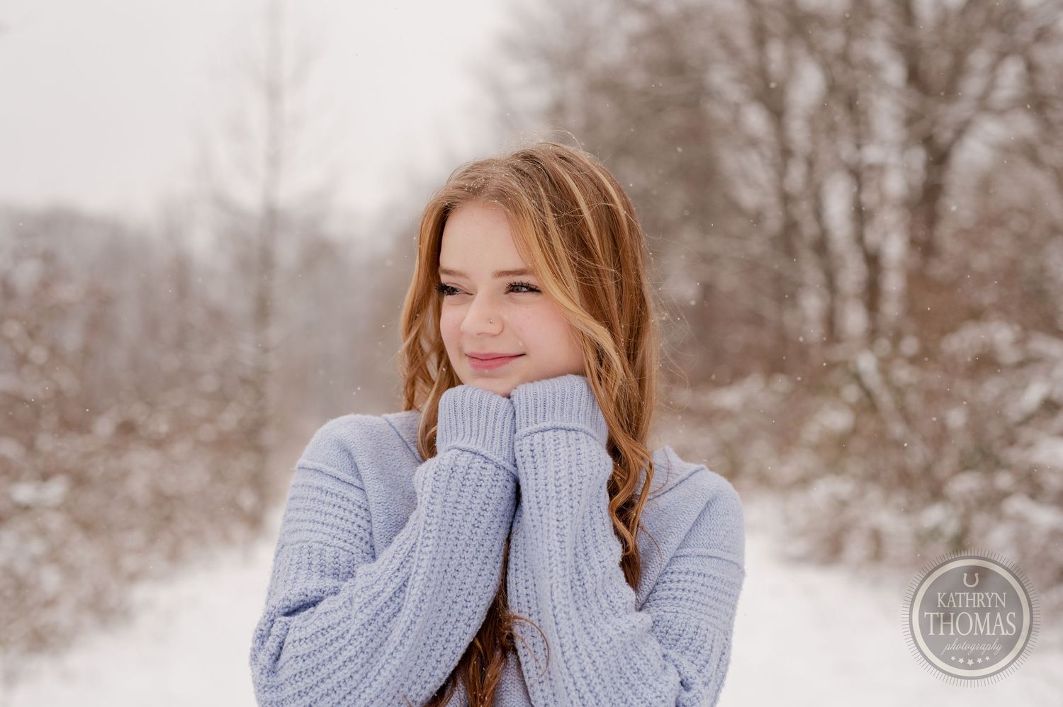 Winter portrait of someone in a chunky knit sweater with hands raised to their face.