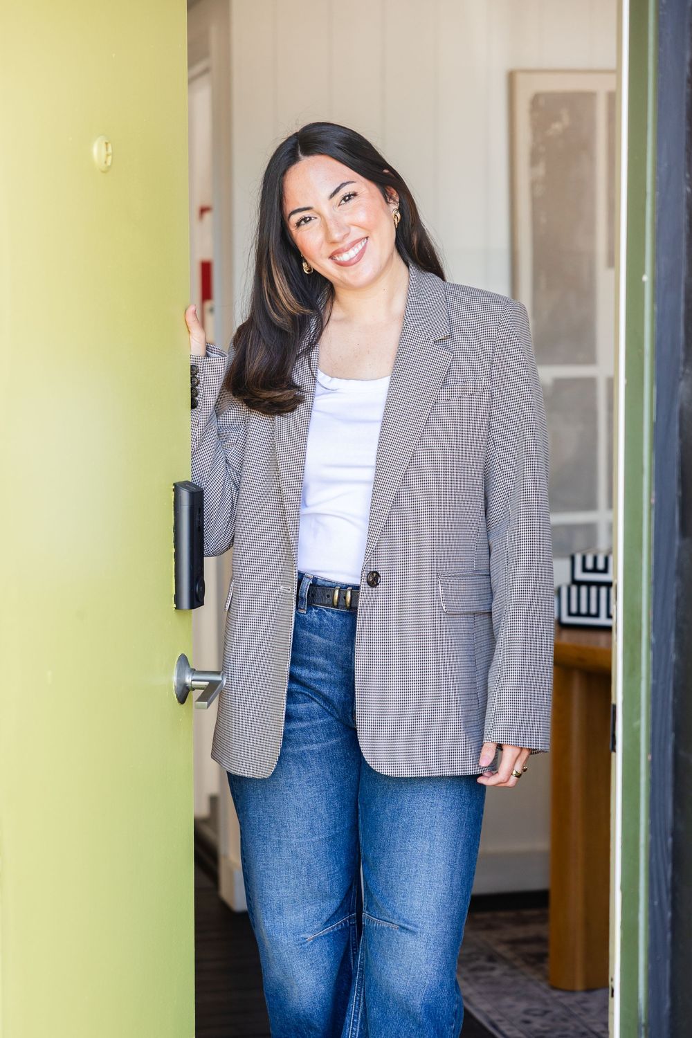 Smiling woman in blazer and jeans standing in open green doorway.