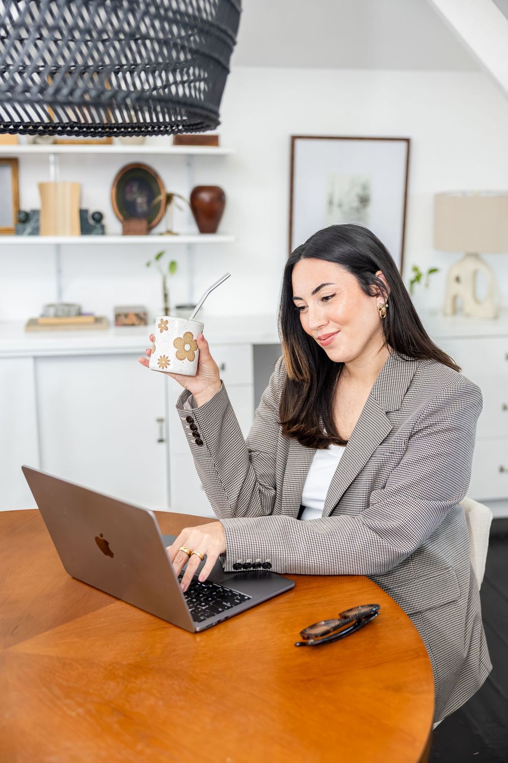 Smiling woman in blazer working on laptop while holding a decorated drink.