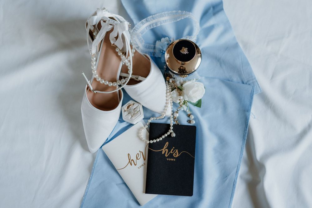 Wedding details flat lay with white heels and his and hers tags on light blue fabric.