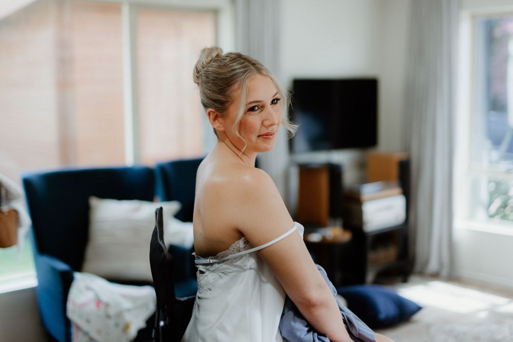 A bride in a classic white wedding dress glances over her shoulder with a happy expression.