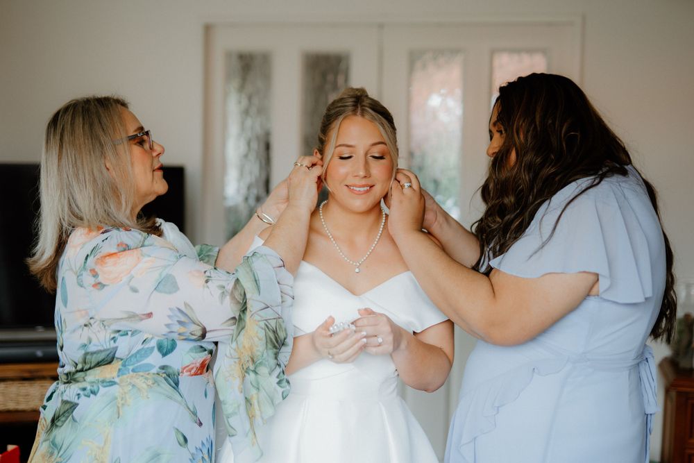 Two helpers assist with final wedding preparations in a sunlit room.