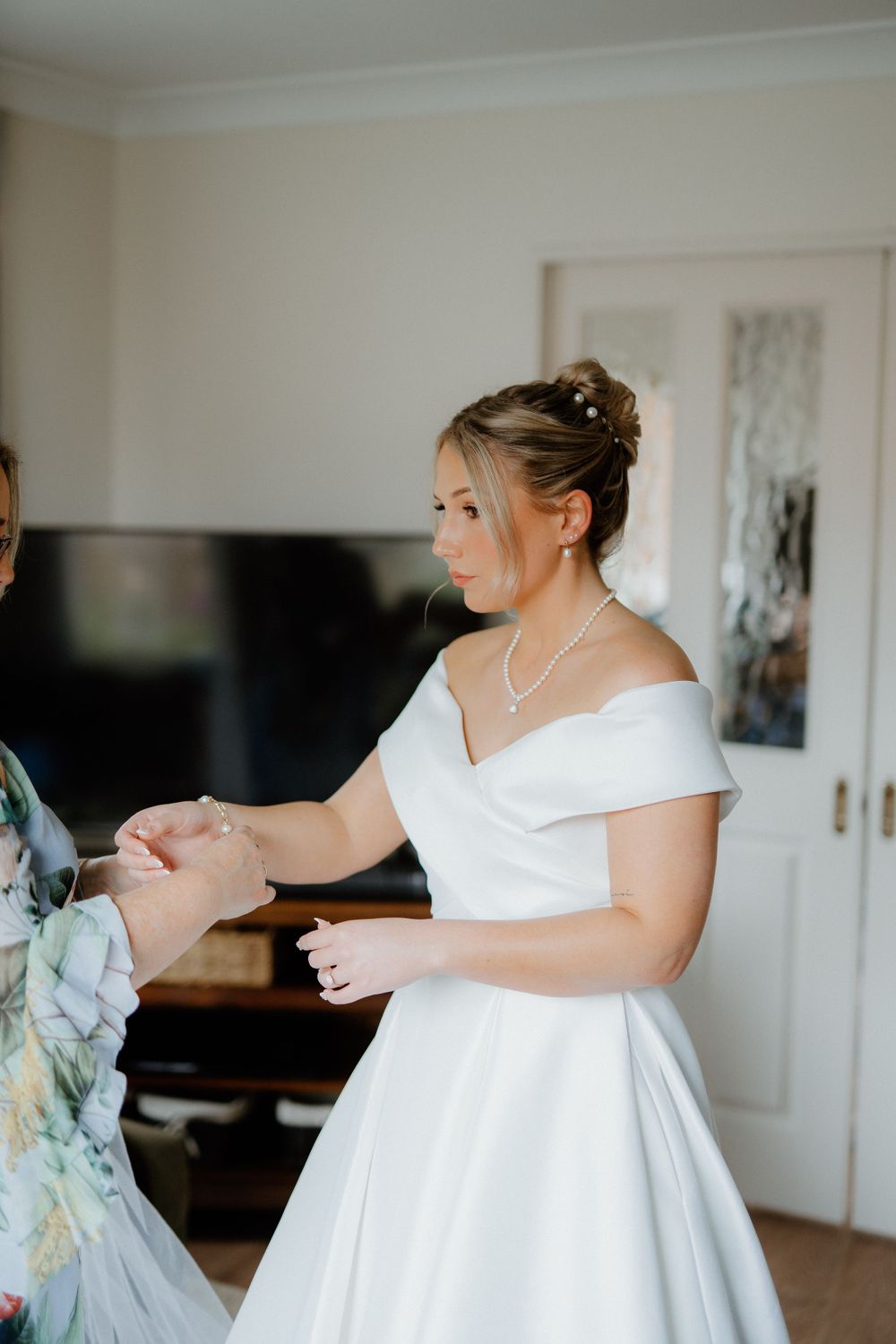A bride in an off-shoulder white gown shares a joyful moment during wedding preparations.