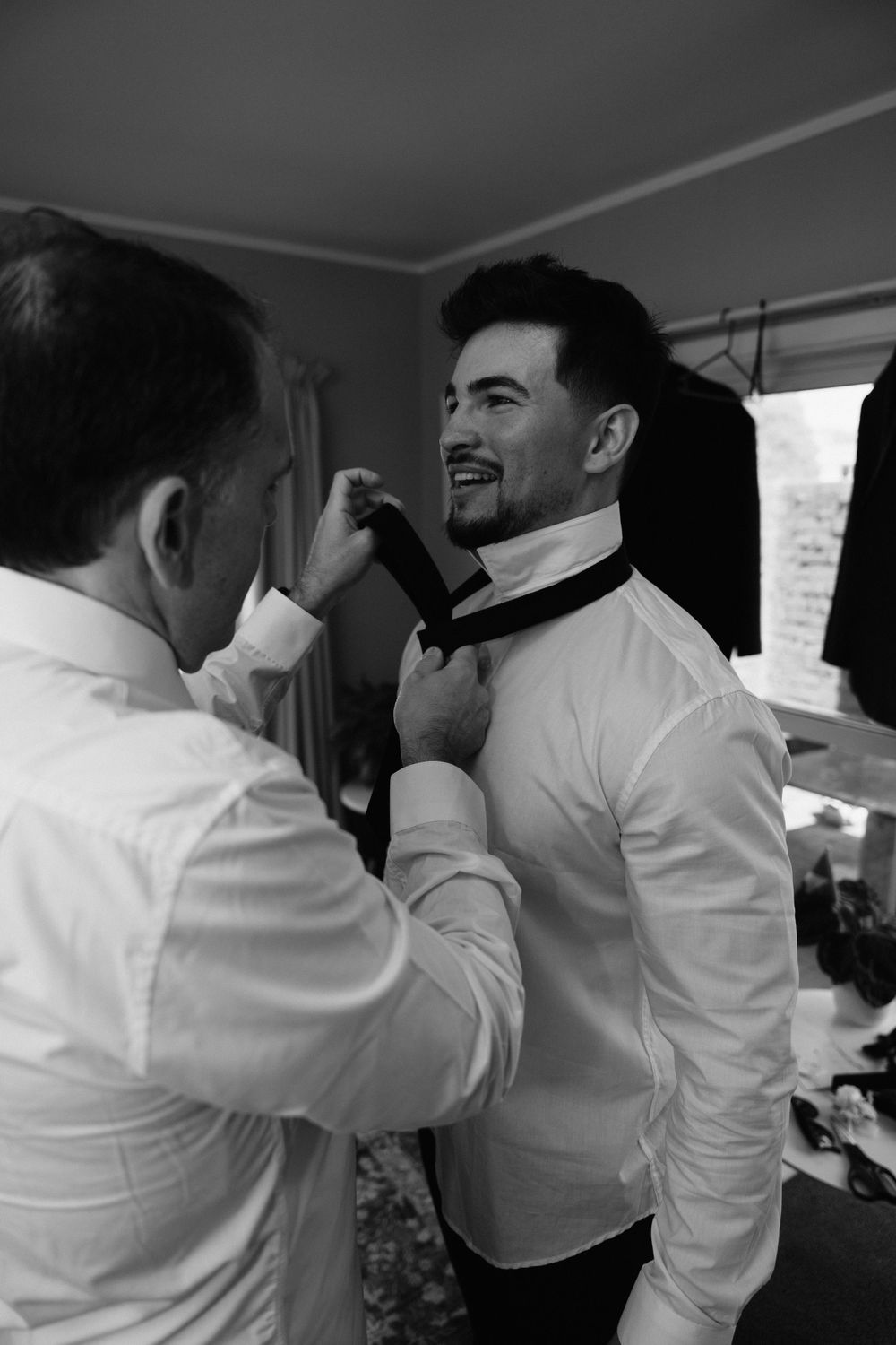 Black and white image of formal bow tie adjustment during wedding preparations.