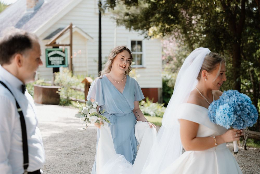 Wedding party members share laughter outdoors with blue hydrangea bouquets.