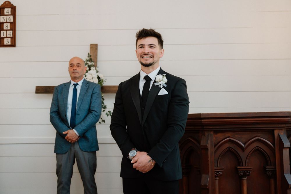 Two men in formal attire stand at attention in a white church interior.
