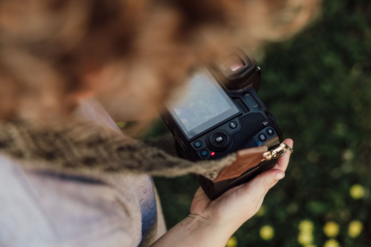 Hands holding small digital camera outdoors with blurred background.