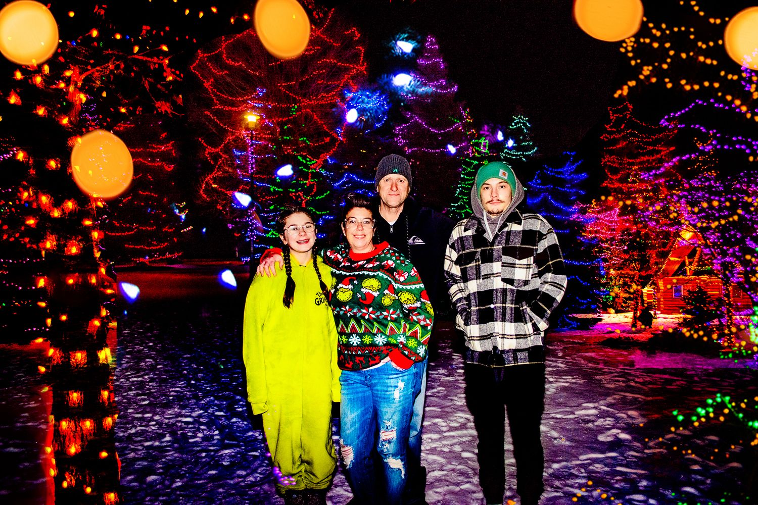 Group standing among colorful holiday light displays at night.