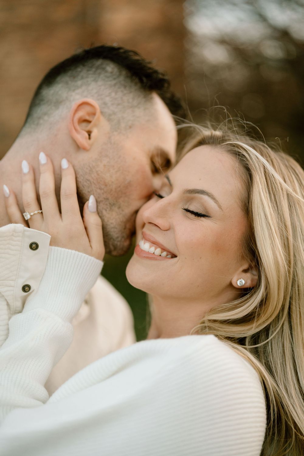 Romantic close-up portrait of couple in white sweaters sharing intimate moment outdoors.