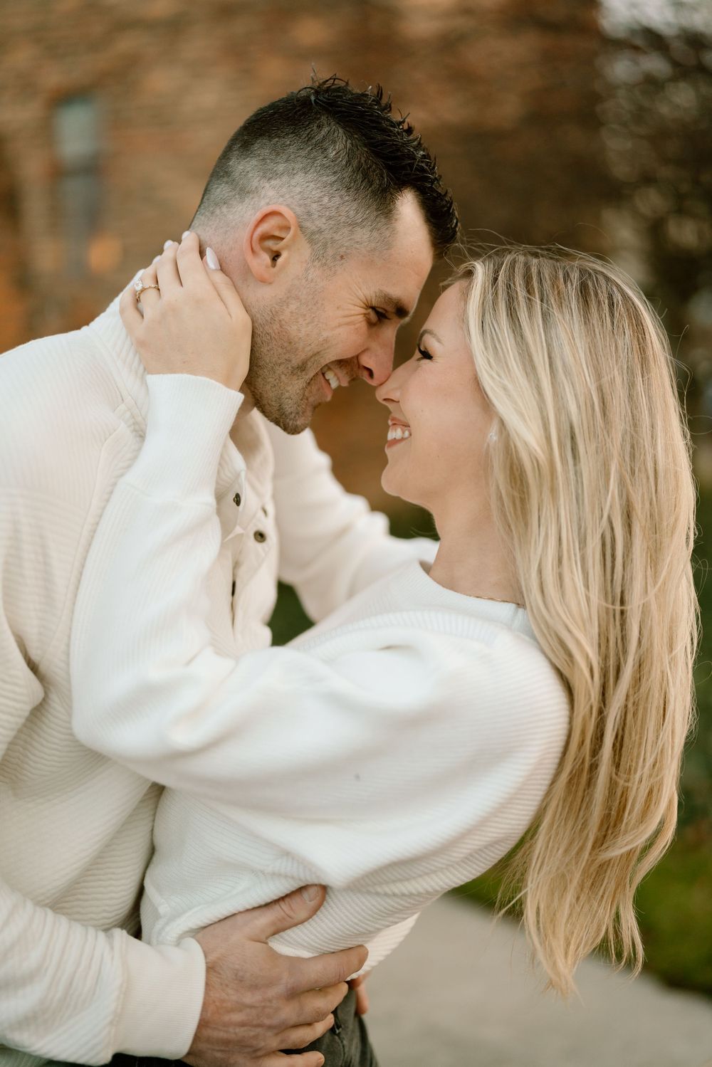 Happy couple embraces while wearing cream sweaters in an intimate outdoor portrait.