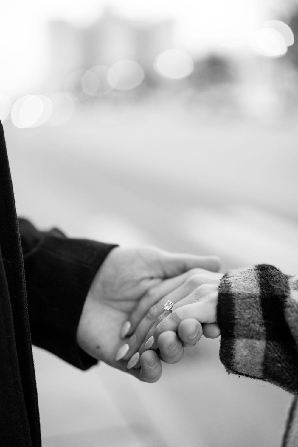 A black and white close-up photo of two hands clasped together, with one wearing a ring and striped sleeve.