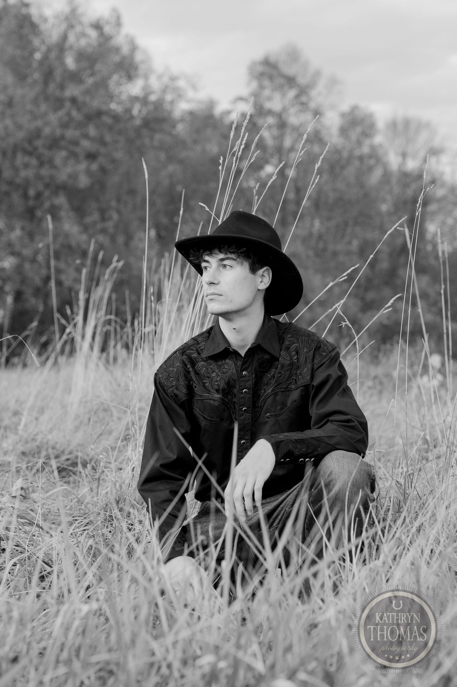 Black and white portrait amid tall grass with trees silhouetted in the background.