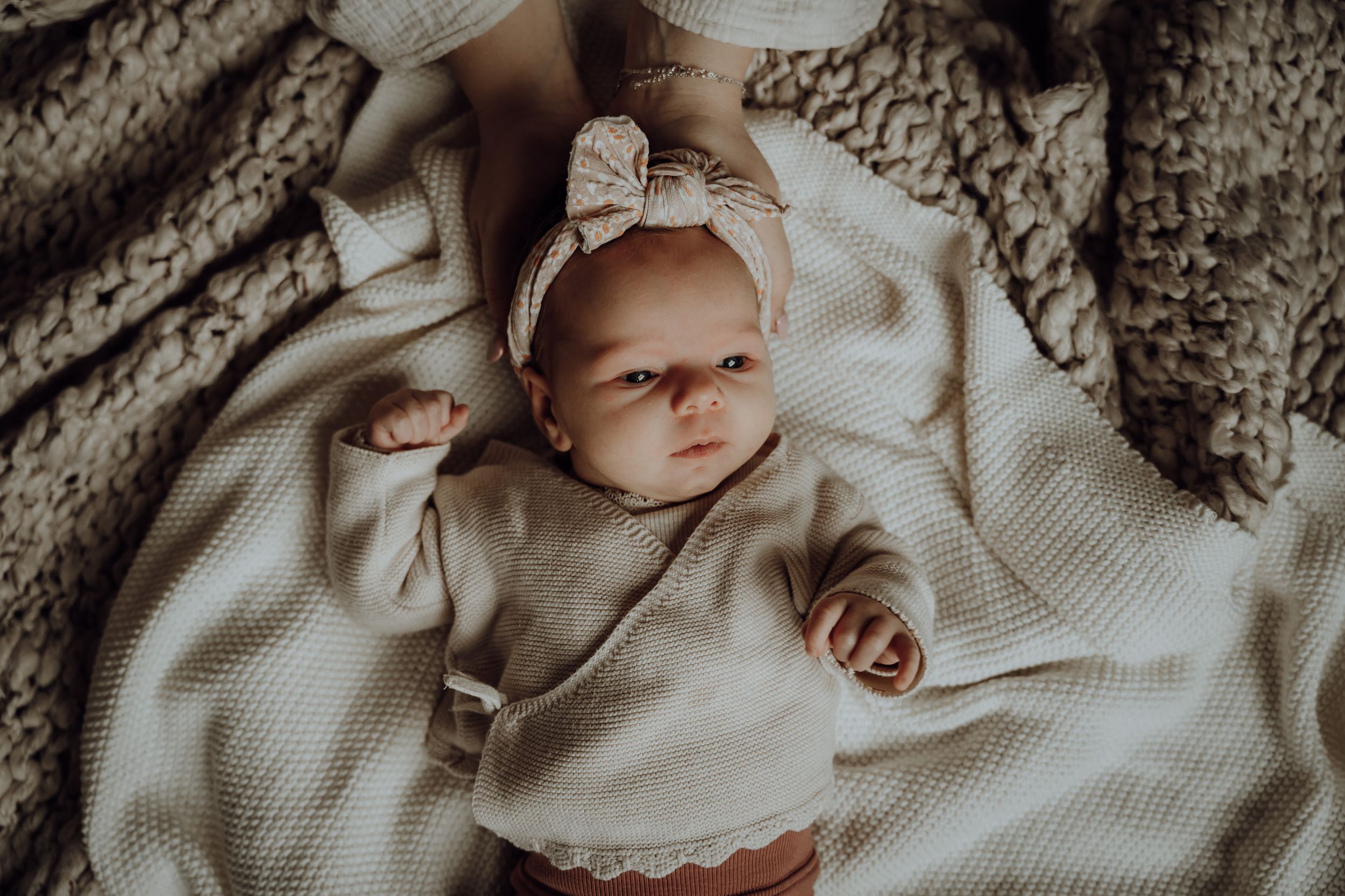 Baby ligt op dekens, vrouw heeft handen in een kommetje waar babyhoofd in rust.