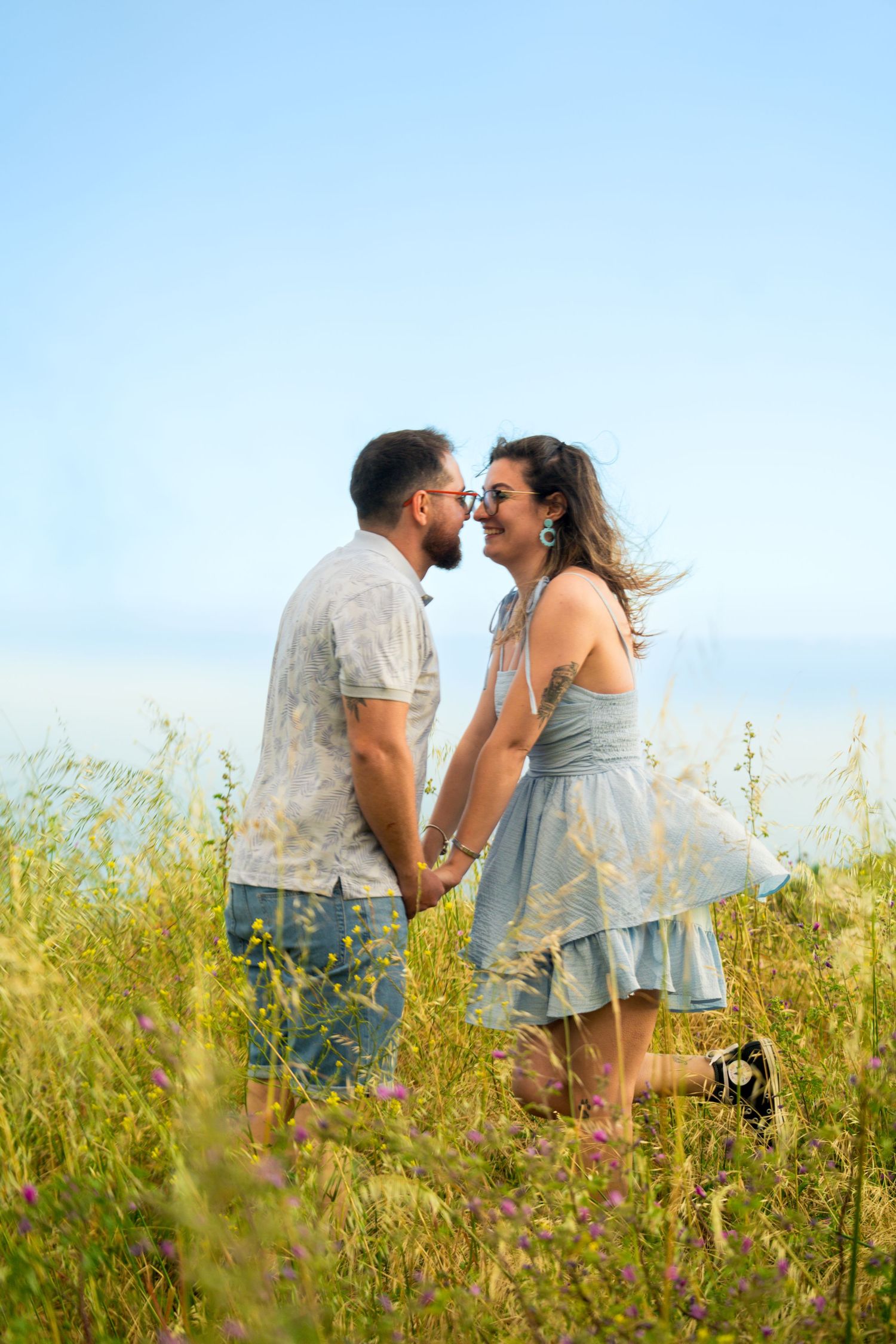 A joyful couple shares a laugh in casual attire among wildflowers on a sunny day.