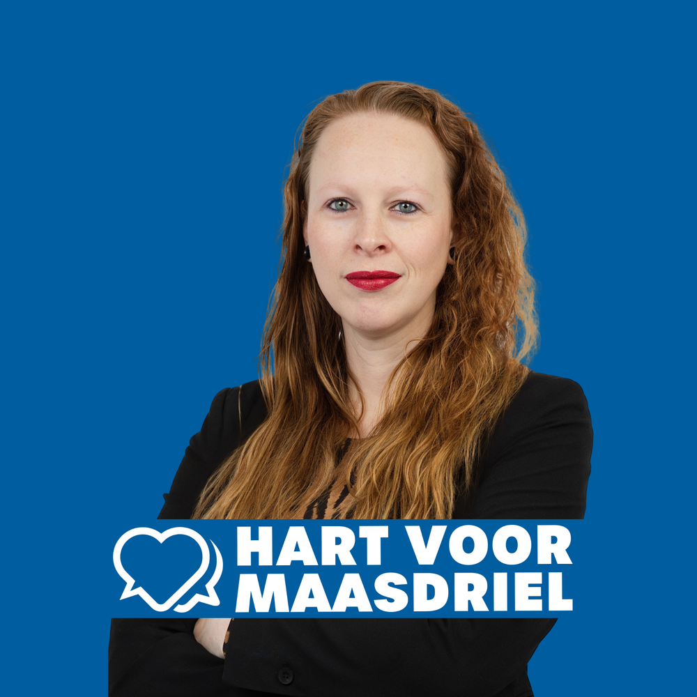 Woman with red hair in black blazer poses for Hart Voor Maasdriel political party portrait on blue background.