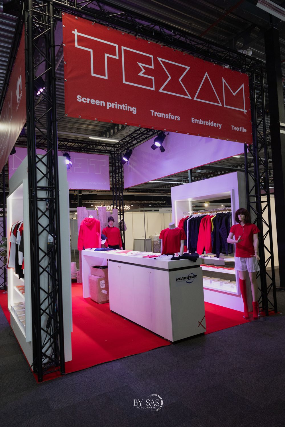 TEXAM trade show booth displaying screen printing, transfers, embroidery, and textile services with red and white apparel displays.