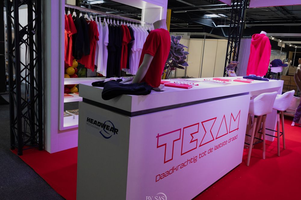 TEXAM branded trade show booth displaying pink and red athletic apparel on mannequins and racks with white display tables.