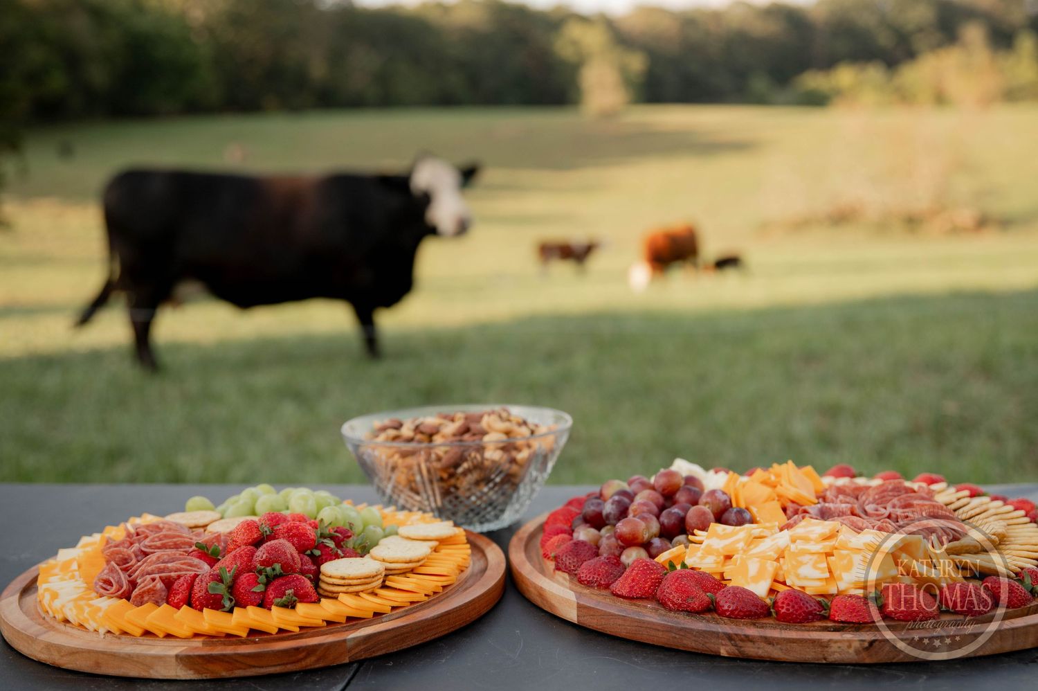 Two elegant wooden charcuterie boards with cheese, salami, grapes, strawberries, and crackers displayed on a table.