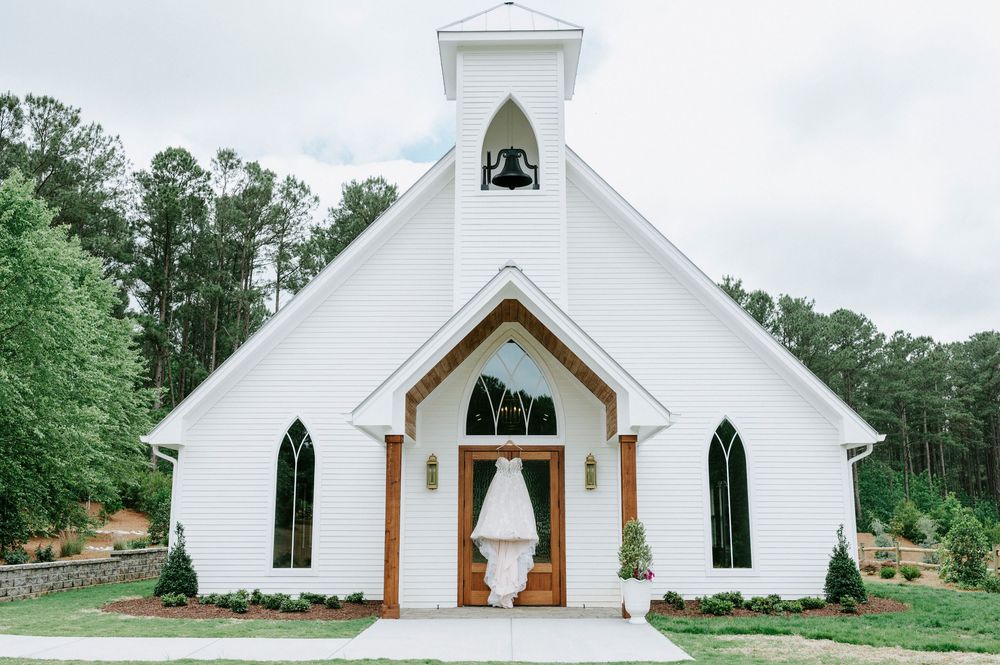 Elegant white chapel wedding venue with gothic windows and bridal gown displayed at entrance.