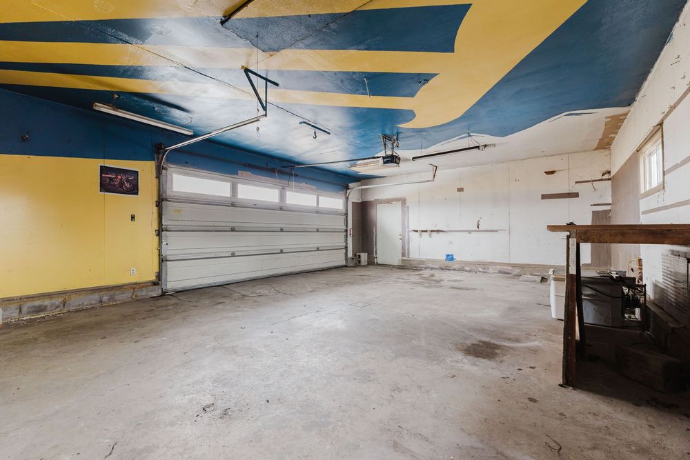 Spacious garage interior with yellow and blue painted ceiling, concrete floor, white garage door, and workbench area.