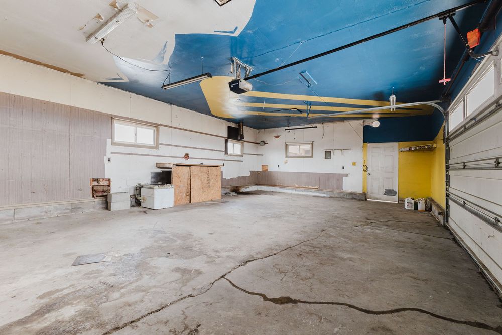 Spacious garage interior with blue painted ceiling, concrete floor, garage door, and workbench area with ample storage space.