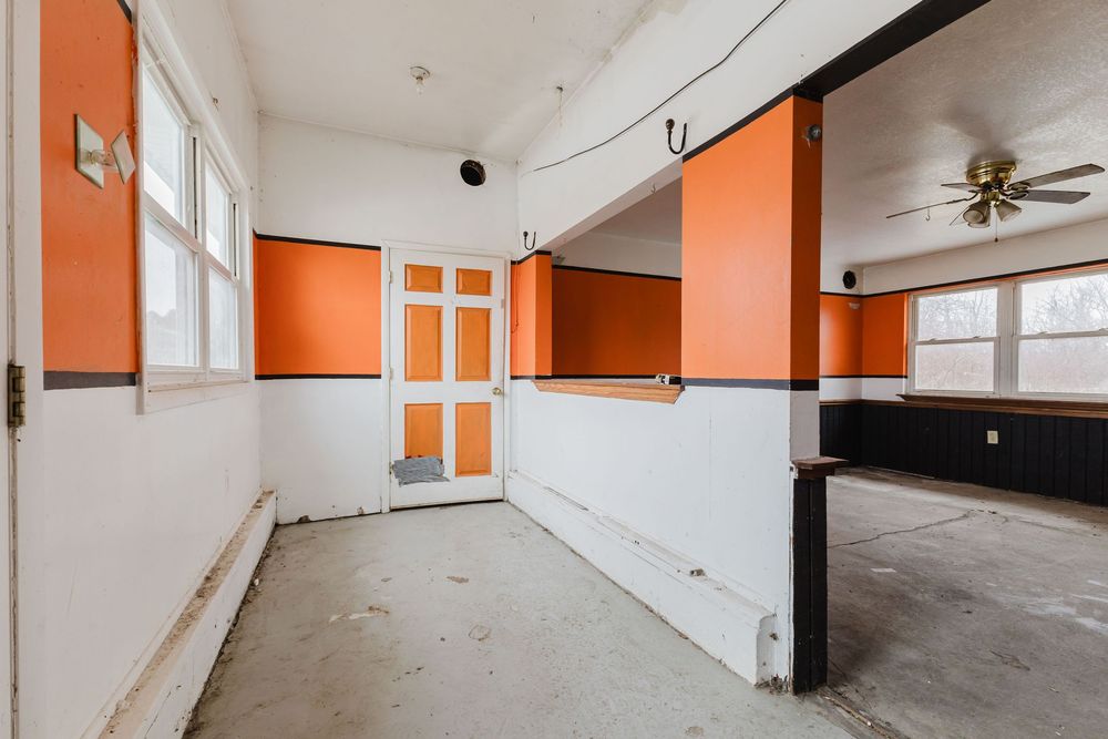 Empty room with bold orange and white walls, concrete floors, ceiling fan, and double doors in a vacant commercial space.