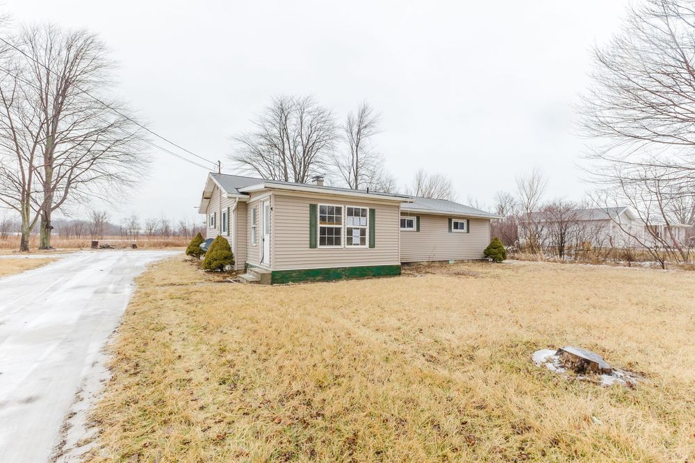 Ranch-style home with green trim, dormant winter lawn, and snow-dusted driveway on a rural property.