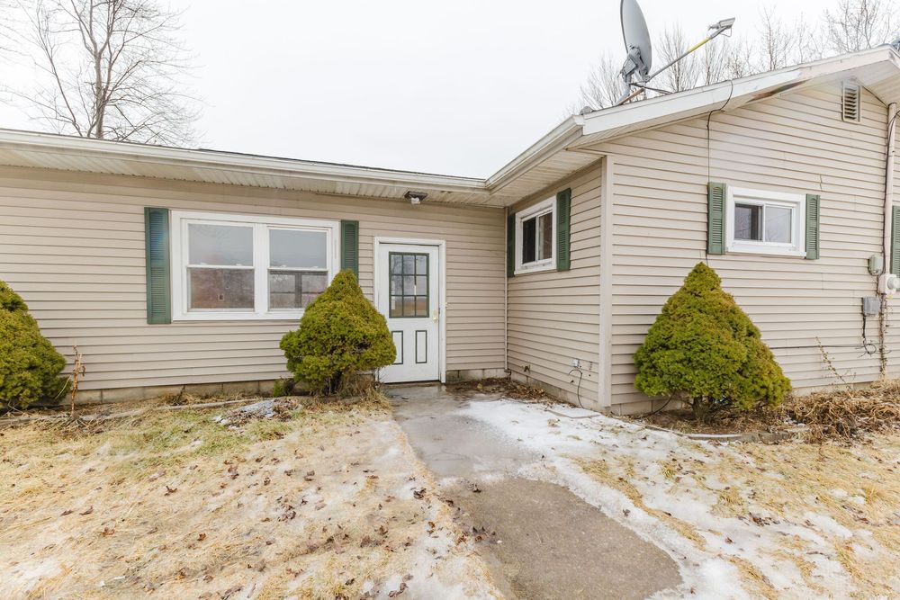 Ranch-style home exterior with beige siding, green shutters, and a concrete path surrounded by snow-dusted ground in winter.