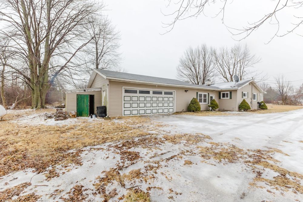 Ranch-style home with attached two-car garage, green shed, and snowy winter landscape in a rural setting.