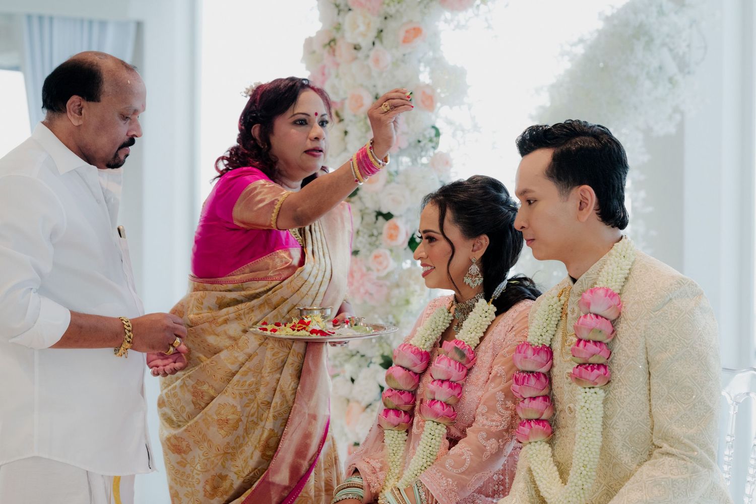 Indian wedding ceremony with guests in traditional attire seated under floral arch by waterfront.