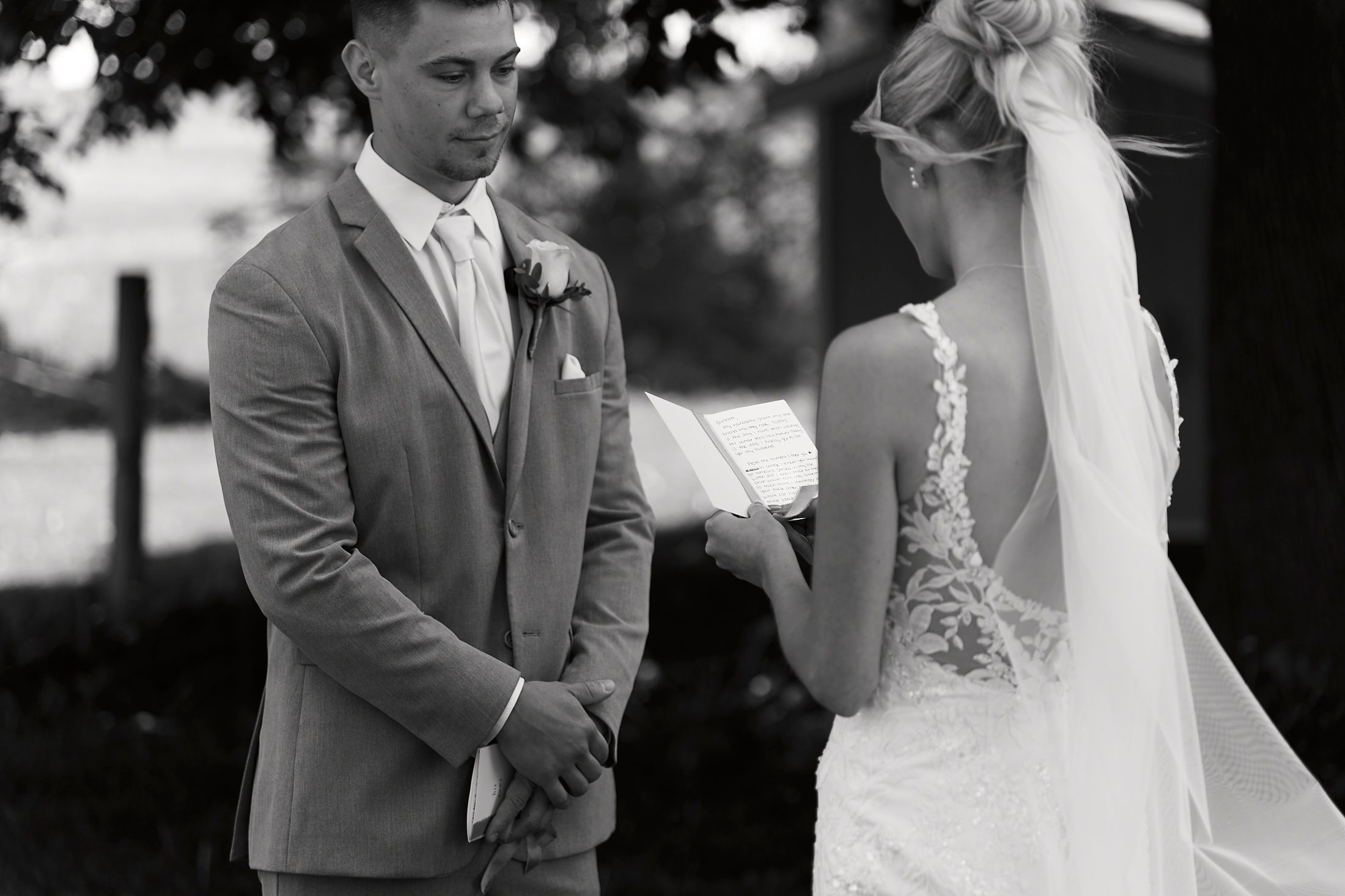 Black and white photo of a groom holding his bride's hands during outdoor wedding ceremony vows.