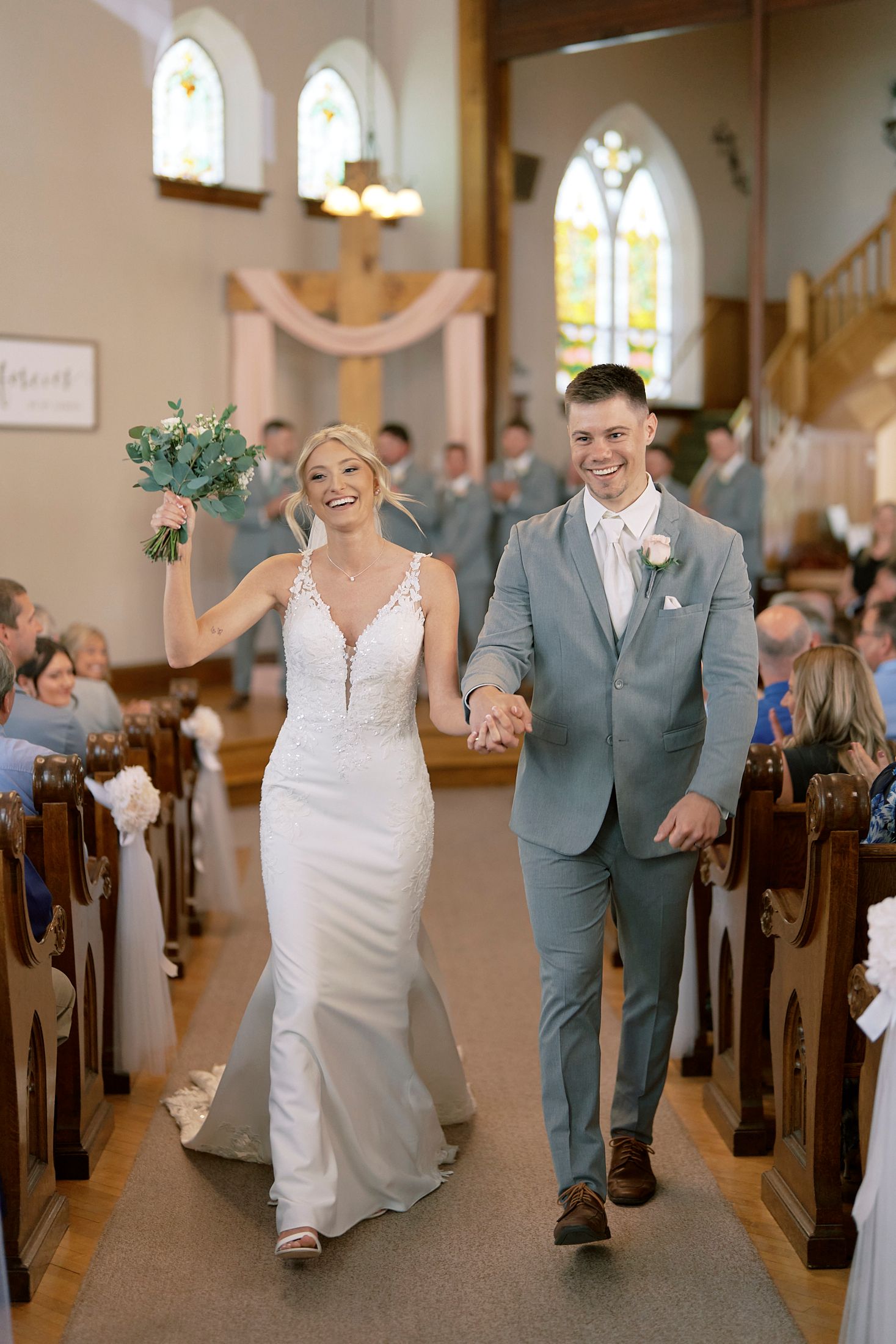 Bride and groom walking down church aisle after wedding ceremony, bride holding bouquet aloft.