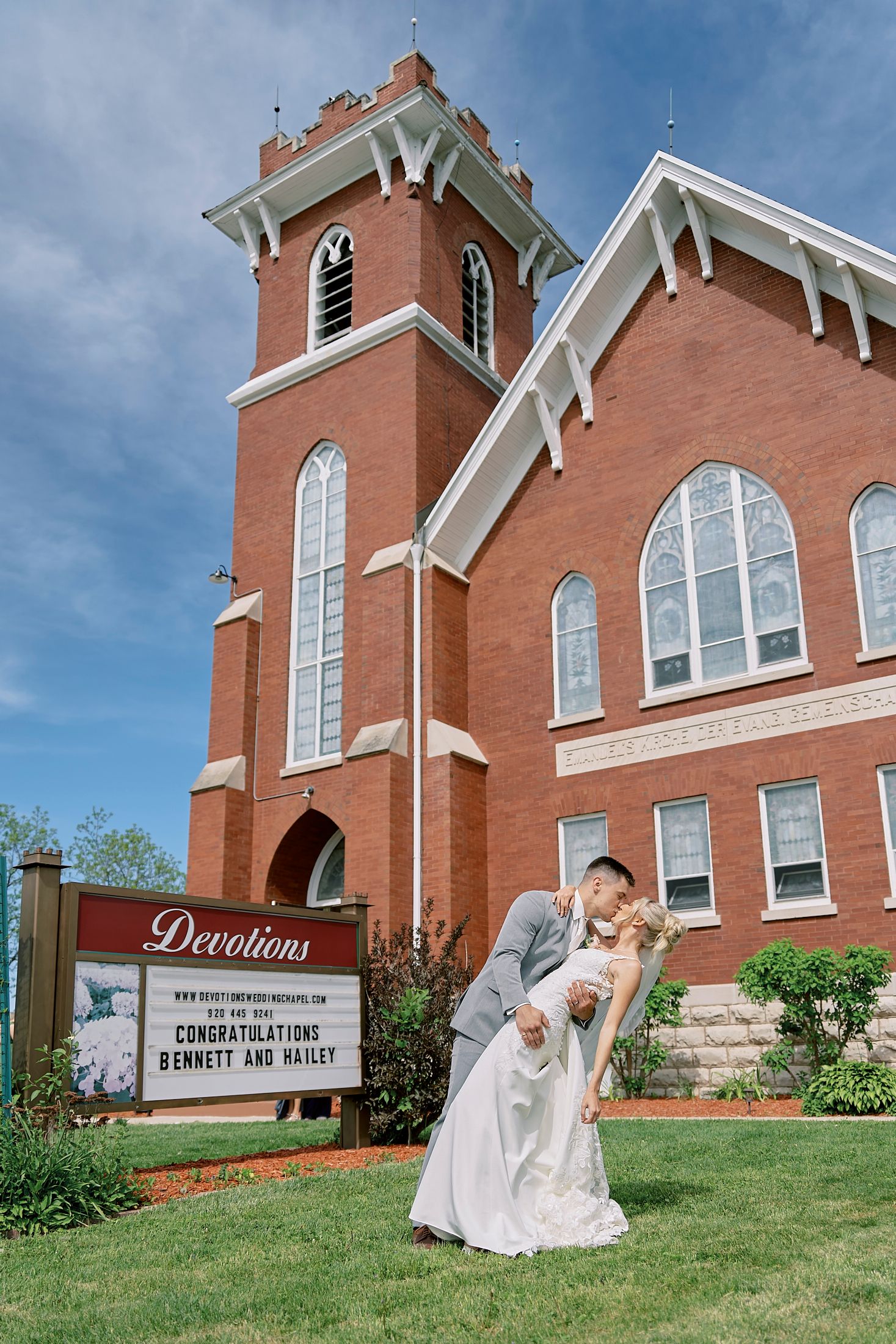 Couple kissing outside Devotions brick church with congratulations sign for Bennett and Hailey.
