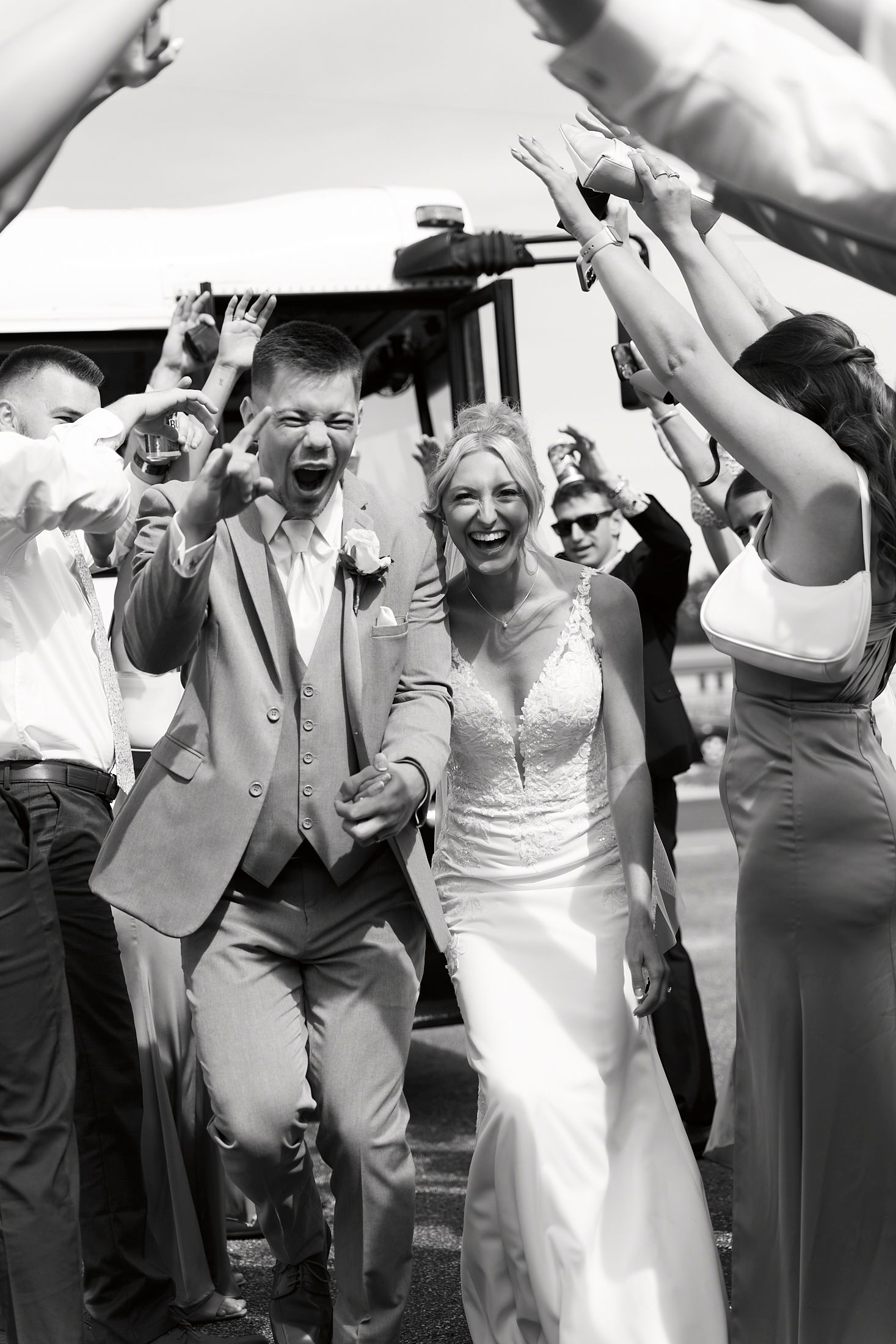 Black and white photo of joyful bride and groom exiting wedding venue through cheering guests.