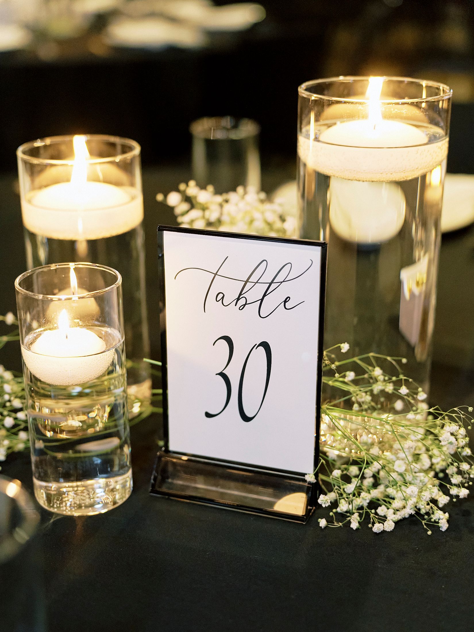 Elegant wedding table centerpiece with floating candles and baby's breath flowers, Table 30 sign.