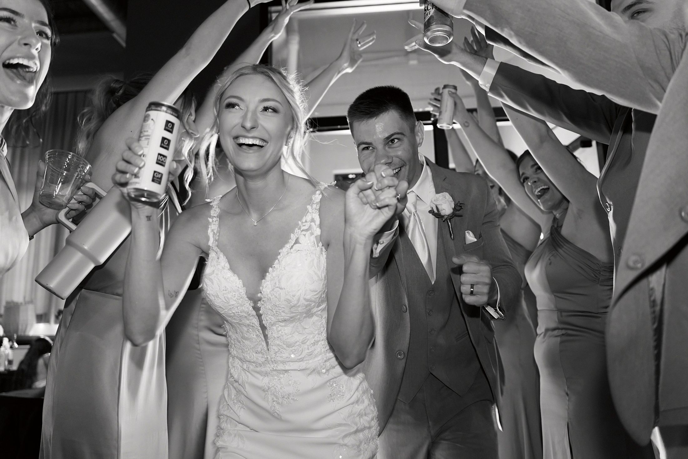 Bride and groom celebrate joyfully walking through a tunnel of raised hands at their wedding reception.