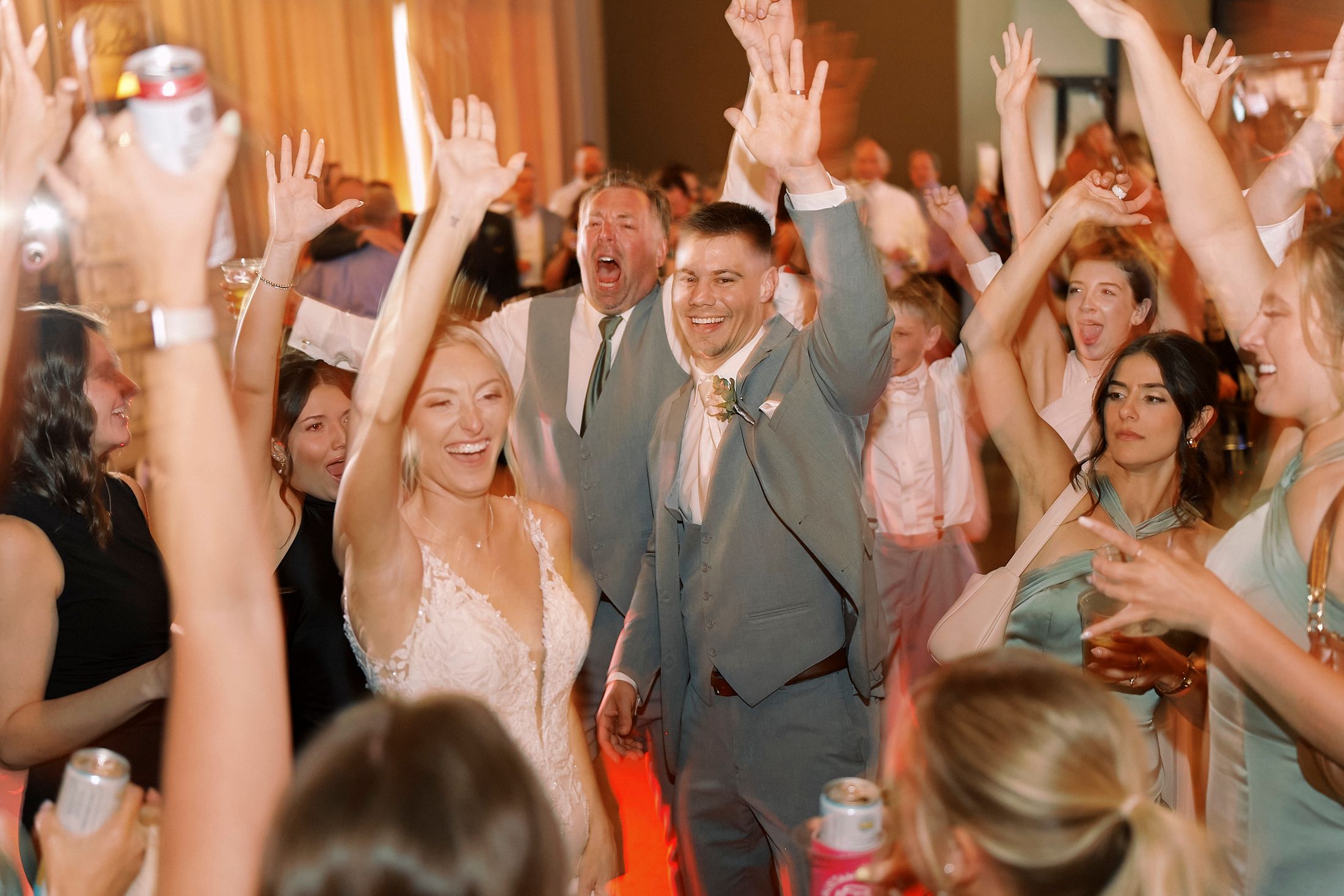 Bride and groom celebrate joyfully on the dance floor surrounded by cheering guests at their wedding reception.