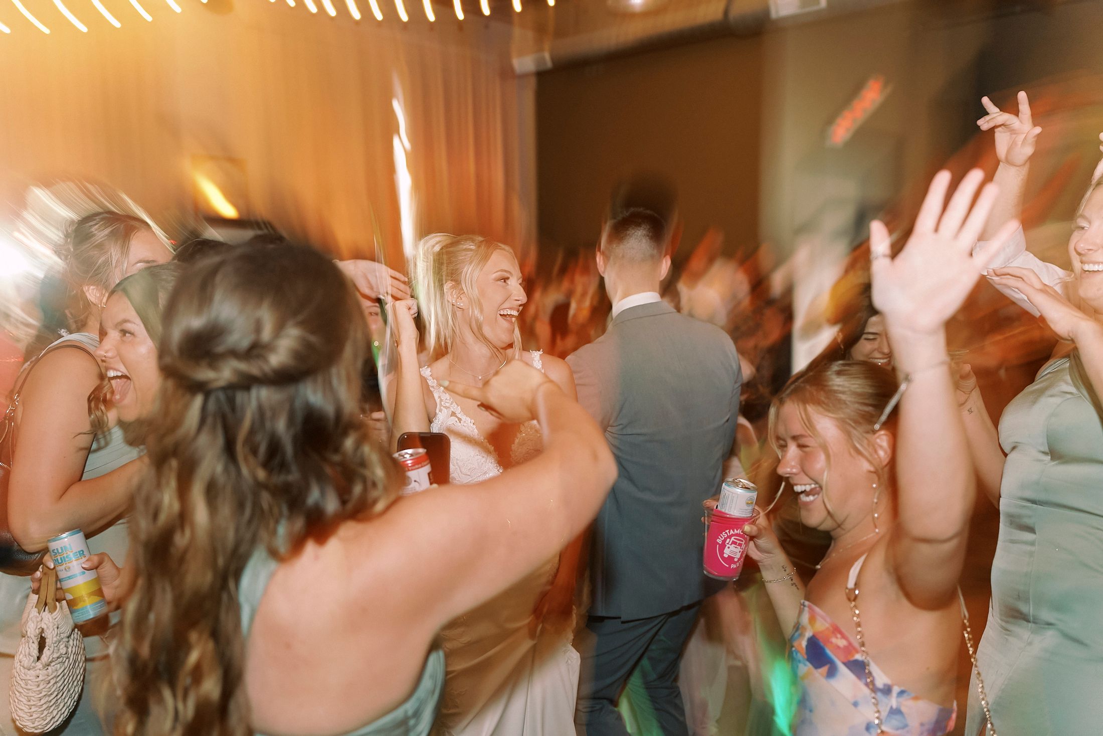 Excited wedding guests dancing and celebrating together on a colorful reception dance floor.