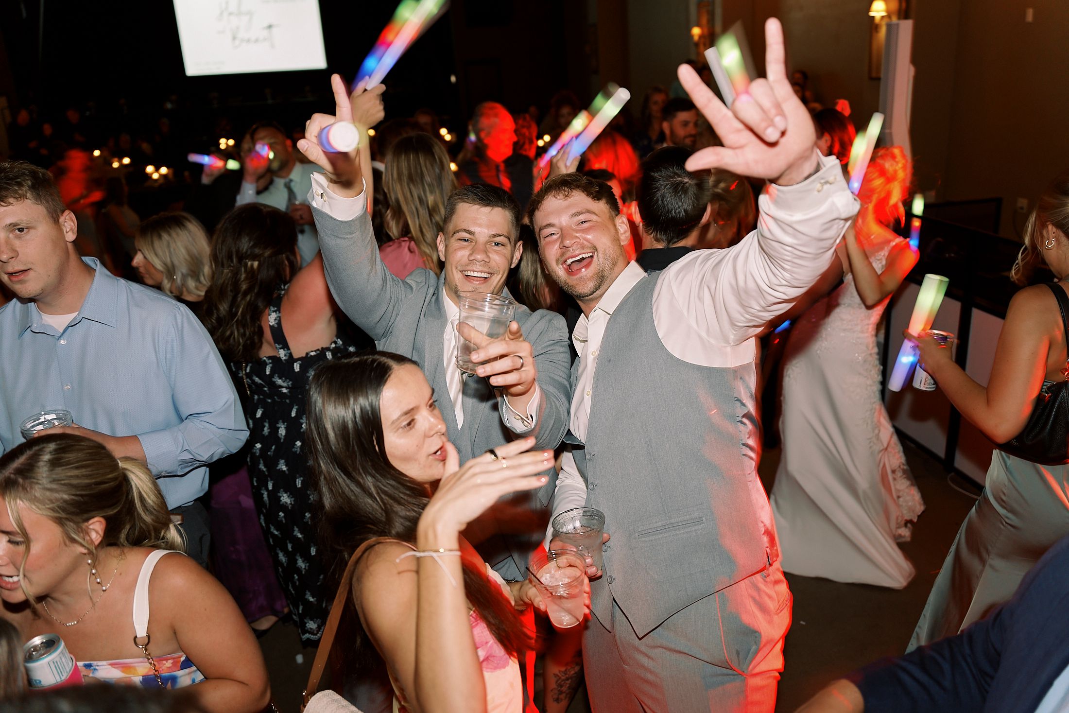 Wedding reception guests dancing and celebrating with colorful glow sticks during lively party.