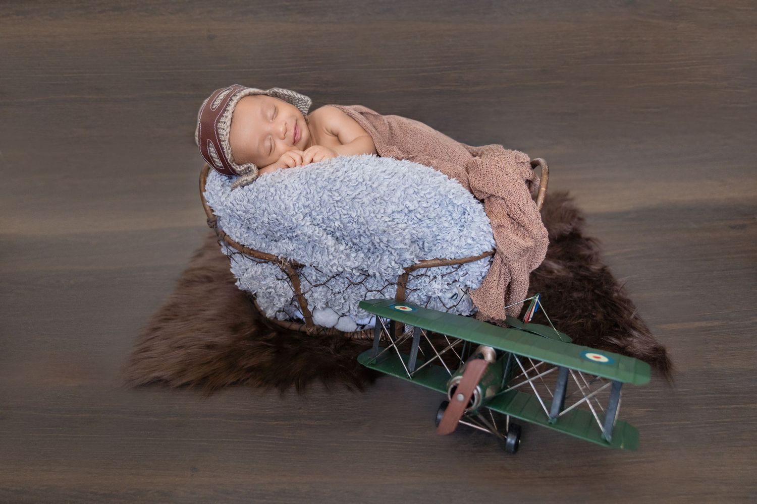 Sleeping newborn baby in aviator hat resting in a wooden crate with a toy green biplane below.