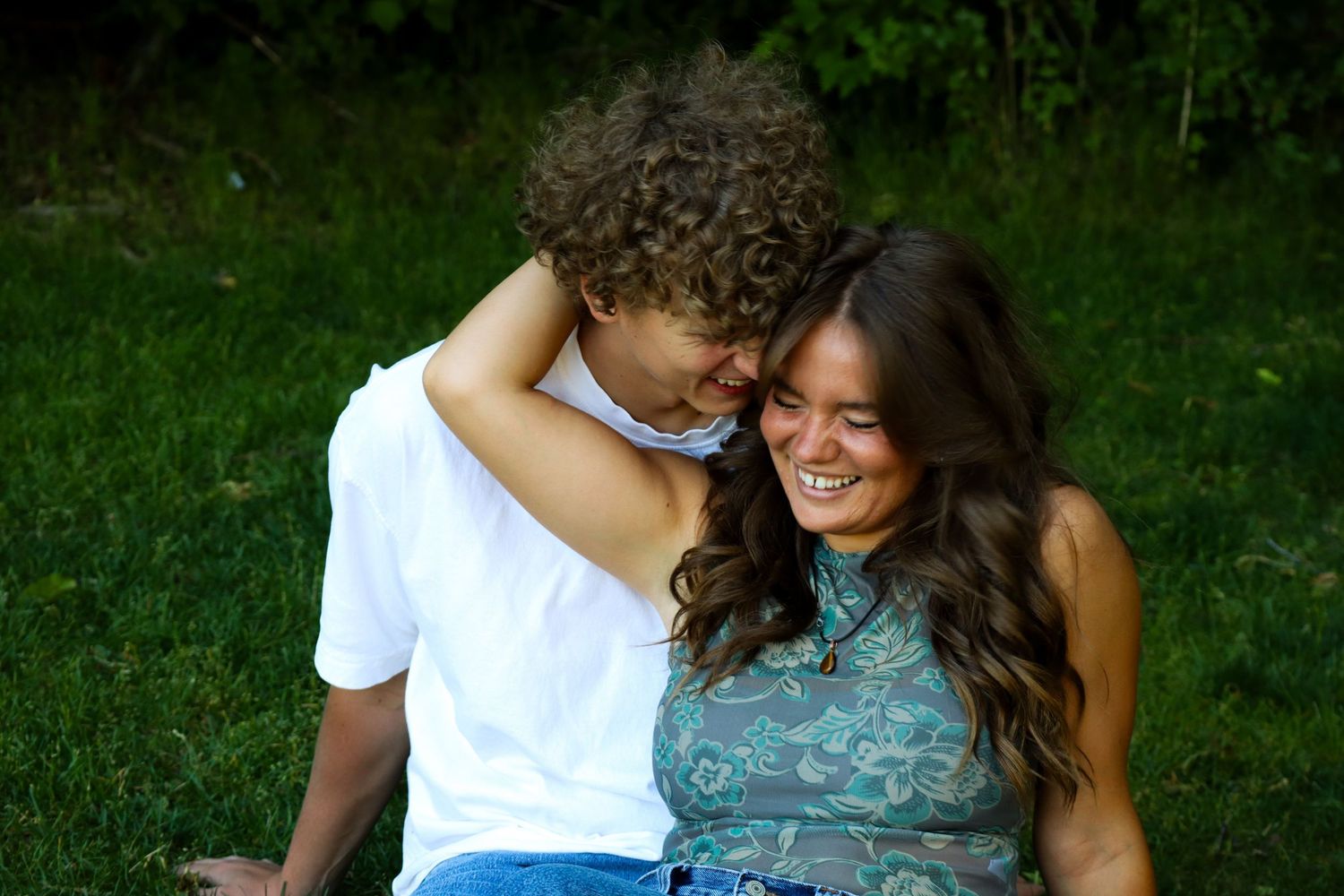 A young woman smiles warmly at a tall young man outdoors on a sunny day near a sports field.