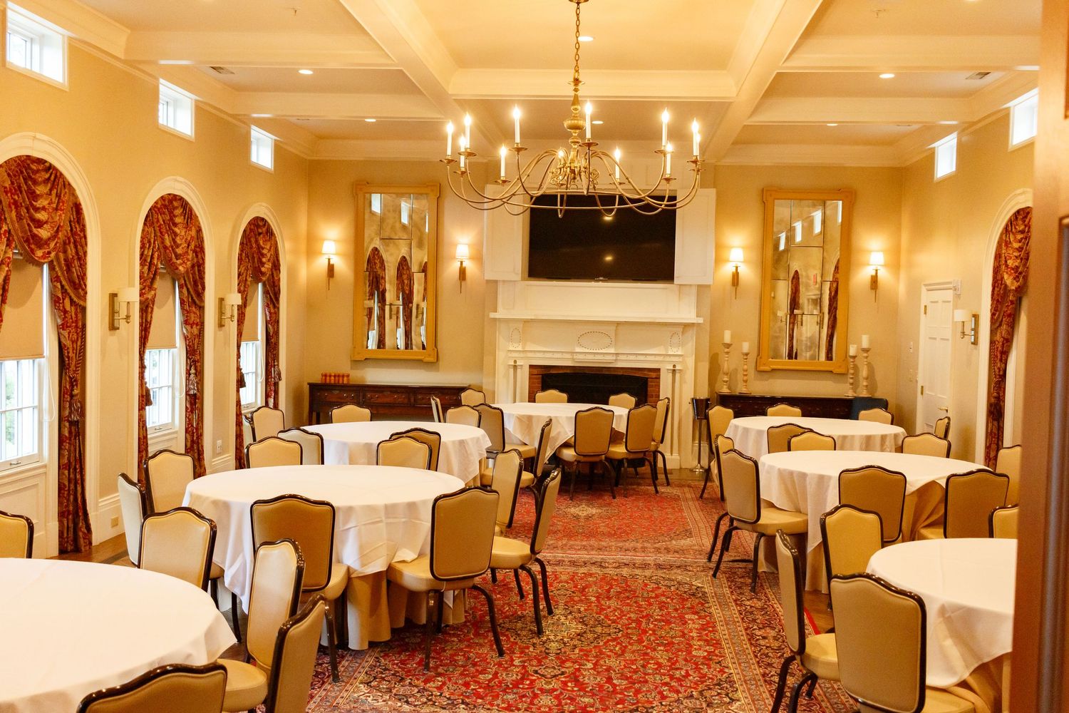 Elegant banquet room with round tables, white linens, chandelier, fireplace, arched windows, and warm gold walls.