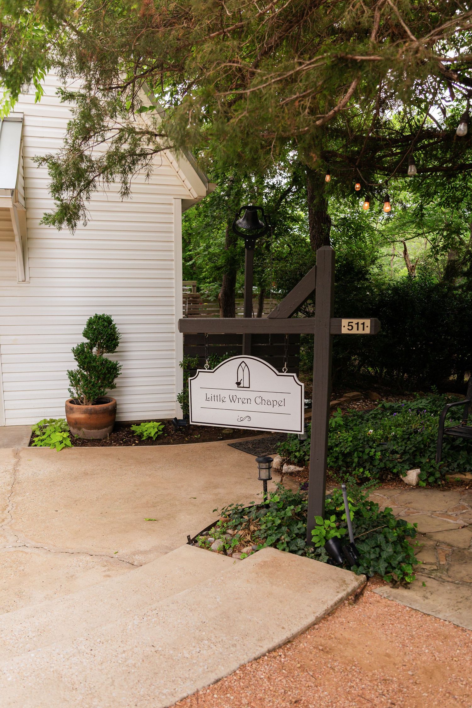 Sign for Little Wren Chapel at address 511, surrounded by lush greenery and manicured shrubs near a white building.