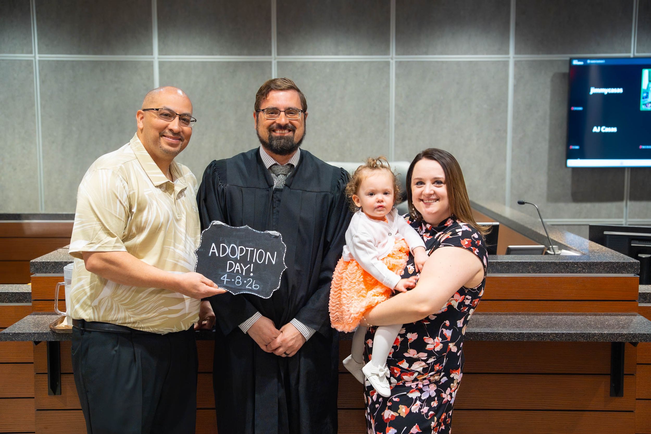 Family celebrates adoption day in courtroom with judge holding chalkboard sign. Quad Cities Event Photography