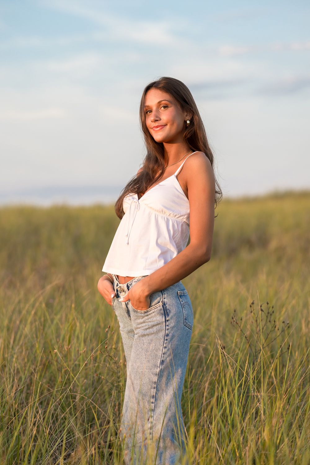 Senior girl poses wearing white tank and blue jeans in coastal grass. North Shore, York, Rye, Gloucester senior photographer
