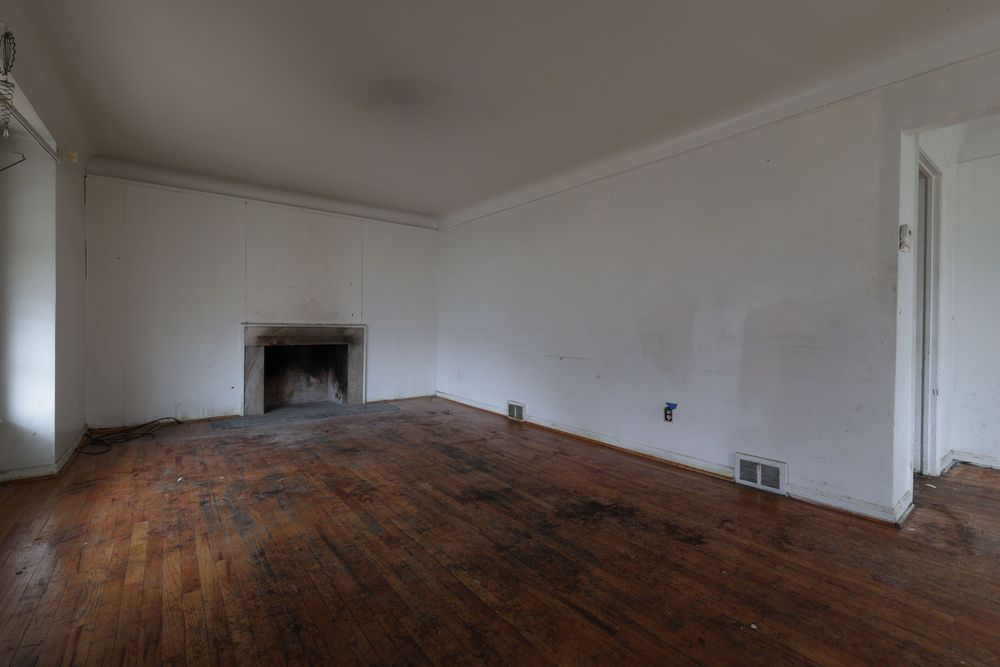 Empty room with hardwood floors, white walls, and a classic fireplace in a vacant residential property.